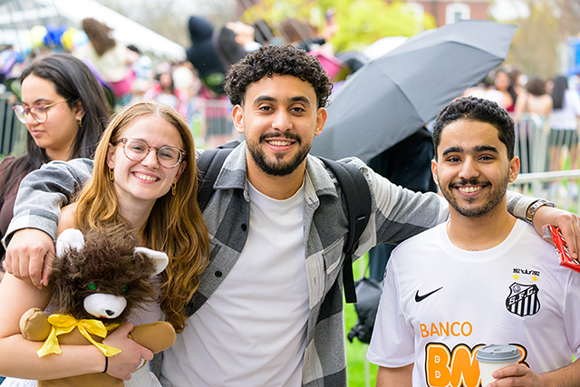 A group of three students at an event with their arms around each other and smiling at the camera.