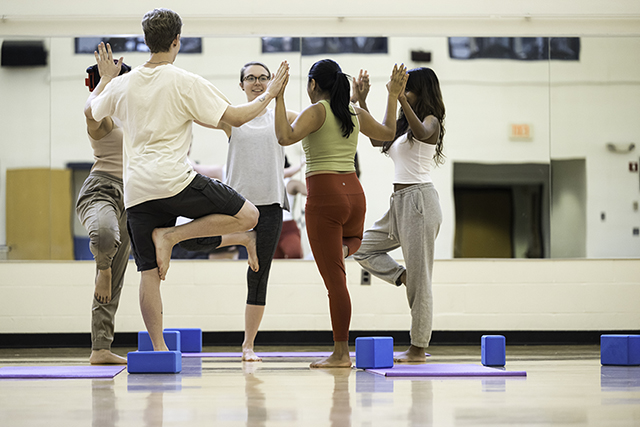 A circle of students practicing a yoga pose in a gym.